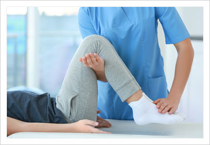 Picture of a female therapist (chest down shot) with one hand under a female patients legs supporting them up while she pushes down on patients feet with the other hand as the patient is lying on her back and her hands next to her side