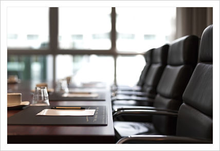 Picture of a board room. There is chairs, a table, papers, pens, and glass cups up side down